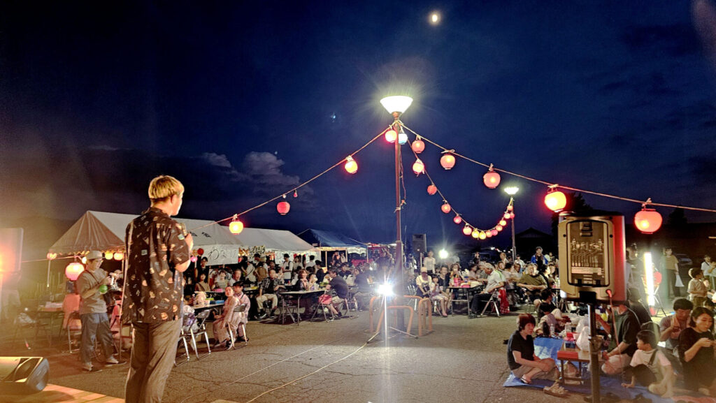 納涼祭でマジックショーを行う様子、提灯の明かりに照らされた夜の会場と観客の賑わい