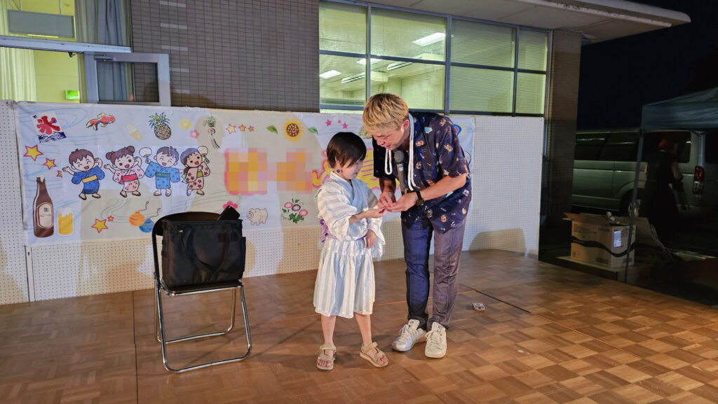 納涼祭のマジックショーで浴衣姿の子どもと一緒にステージで手品を披露する様子