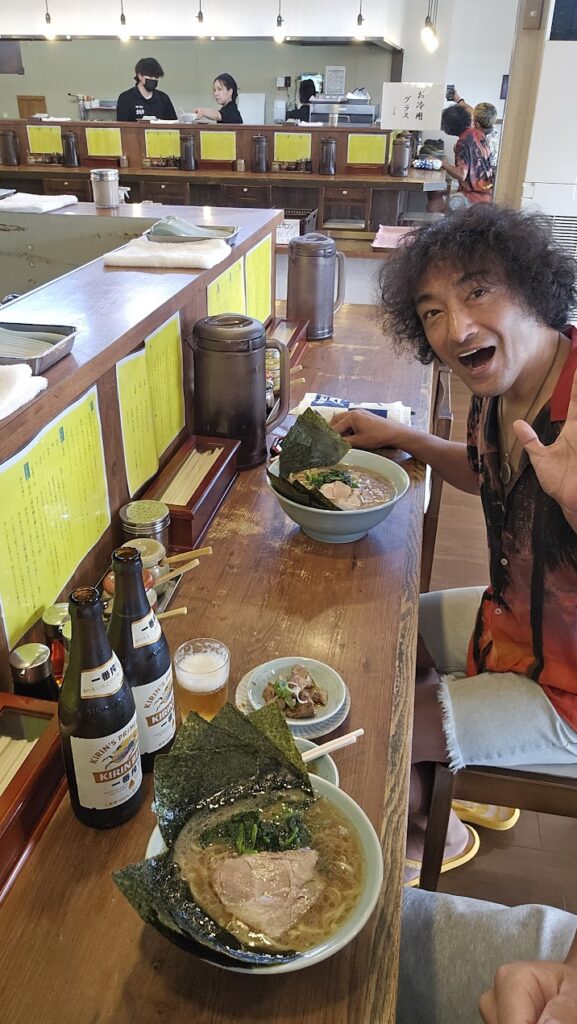 快気祝いの場面で、幼馴染と一緒に横浜家系ラーメン 元喜家 高岡店のカウンター席に並び、チャーシュー麺とビール、小皿料理を楽しむ様子。笑顔と元気があふれる一枚。