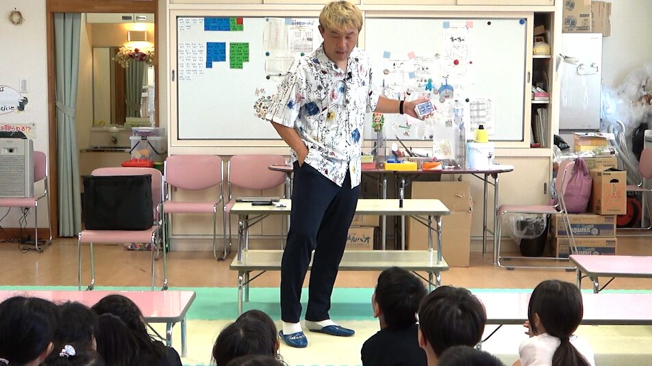 学童保育のマジックショーでトランプマジックを披露するマジシャンコンプレッサーと見守る子どもたち