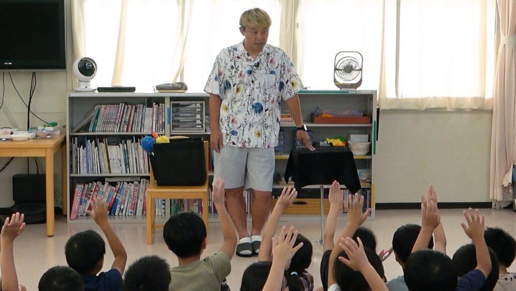 高岡市の学童保育でのマジックショー。コンプレッサーの問いかけに子どもたちが元気よく手を挙げている様子。