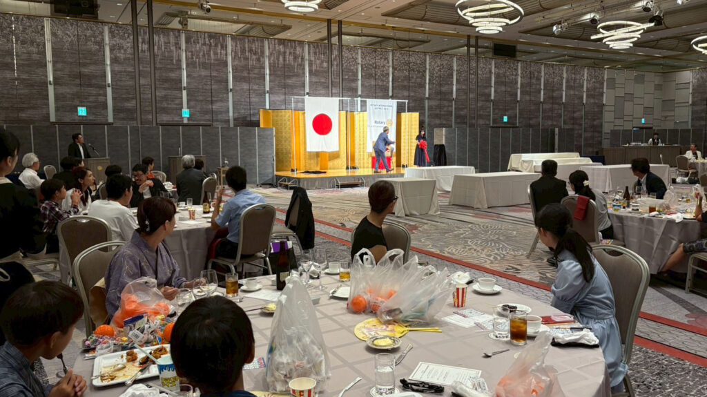 金沢ロータリークラブのパーティーでホテル日航金沢の大広間に設けられたステージ前で行われたマジックショーの様子。観客が円卓に座りながらショーを楽しんでいる。