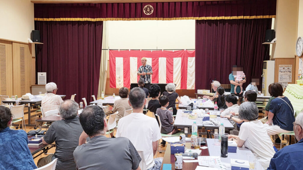 「富山 出張マジックショー 高岡市納涼祭の公民館ホールでの舞台風景、観客が見守る中マジシャンが演技を披露