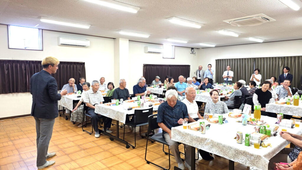 富山県高岡市の敬老会で、参加者と気さくにコミュニケーションをとりながらマジックを披露するコンプレッサー。会場はおしゃべりマジックによって笑顔と一体感に包まれている。