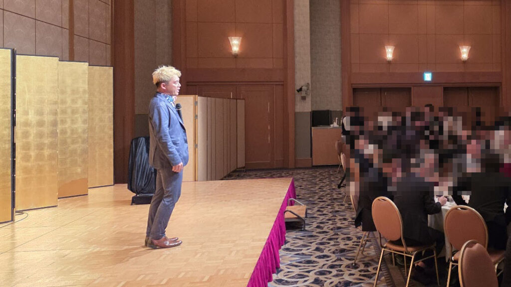 富山のパーティー会場（ANAクラウンプラザホテル富山）のステージで、参加者に向けて語りかけるマジシャン・コンプレッサー。