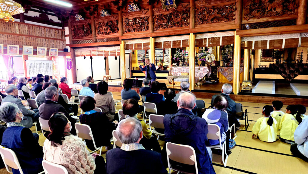 お寺の畳の上で、マジックショーを真剣に見つめる保育園児（子供）たちと、その横に座るお年寄りの観客。