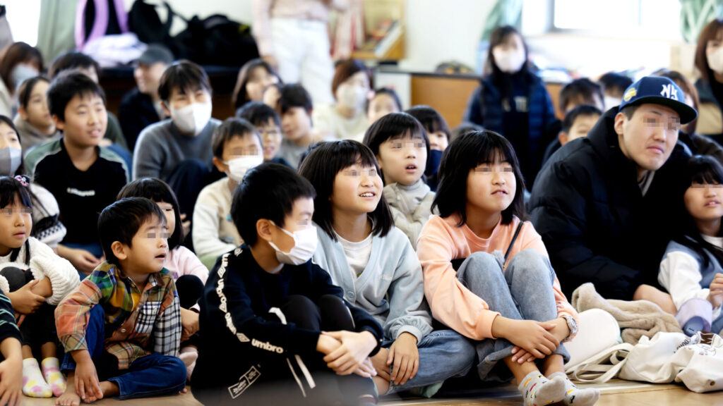 富山のクリスマス会でマジックショー!プロの写真とAIの活用術。 2 マジックショーに夢中になり、目を輝かせてステージを見つめる子供たちのアップ。驚きと楽しさが入り混じった純粋なリアクションが、会場の熱量を伝えている。