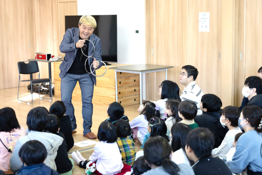 富山のクリスマス会でマジックショー!プロの写真とAIの活用術。 3 リンキングリングマジックを披露し、子供たちの目の前で不思議な現象を見せるコンプレッサー。身を乗り出して驚く子供たちと、一体感のあるショーの様子。