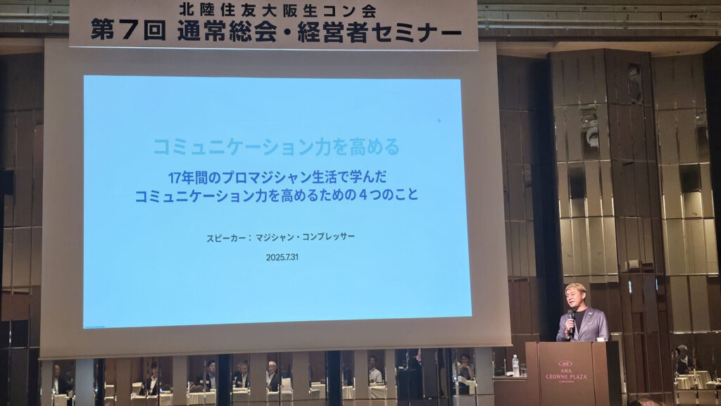 講演をしているプロマジシャン　コンプレッサー。スクリーンには「コミュニケーション力を高める」と書いてある。
