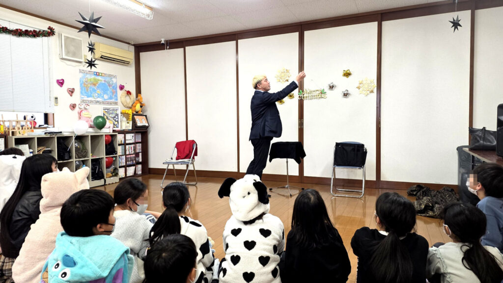 氷見市の学童保育で開催されたクリスマス会で、マジックを披露して子供たちを驚かせるマジシャン・コンプレッサーの様子