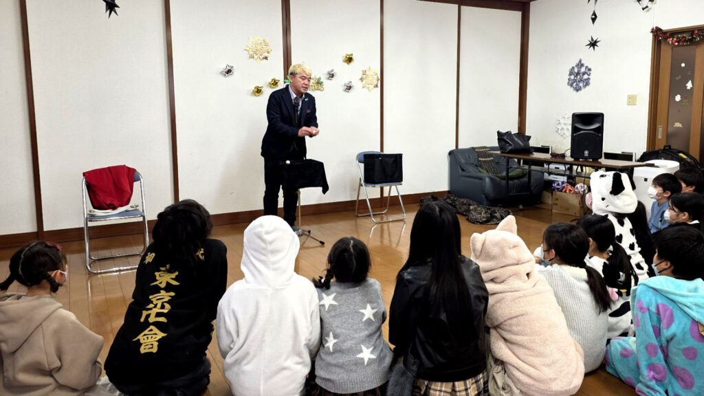 氷見市の学童保育で開催されたクリスマス会で、マジックを披露して子供たちを驚かせるマジシャン・コンプレッサーの様子
