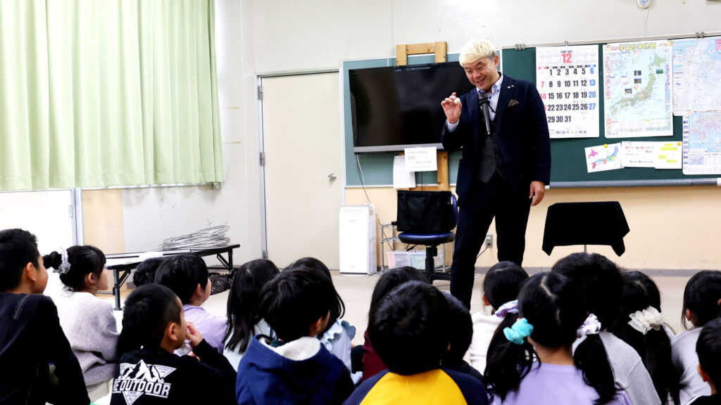 ステージ上で不思議な現象を実演し、子供たちが身を乗り出して見入るマジックショーのワンシーン