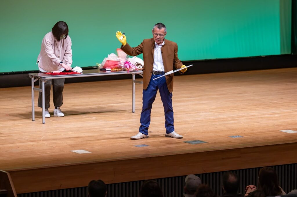 富山出身のマジシャン　アレマー玉井さんが観客をステージにあげて超能力マジックを演じている