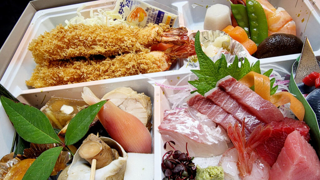 料亭「茜月」で提供された、色鮮やかで豪華な会食のお料理。お刺身や海老フライなど、お子様から大人まで楽しめるお弁当。