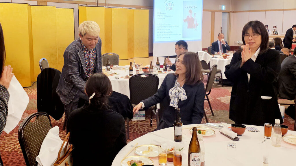 グランテラス富山の新年会でテーブルマジックを披露するマジシャンコンプレッサー。至近距離での不思議な現象に笑顔で反応する女性ゲスト。