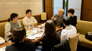 高岡「カジュアルダイニング BON」でテーブルマジックを披露するマジシャン・コンプレッサー。花柄シャツを着て、テーブルを囲む大人と子供たちに間近でマジックを見せている様子