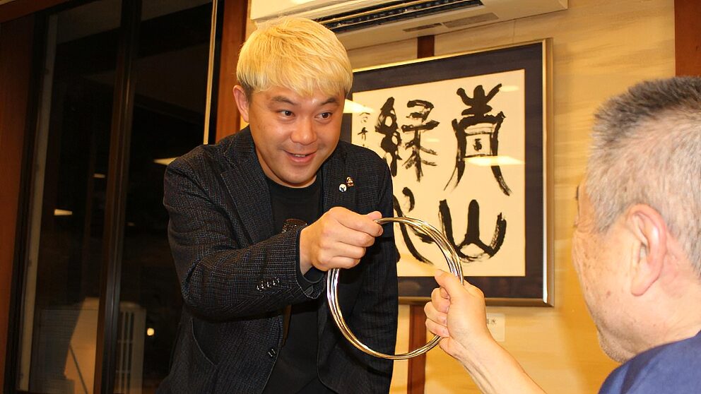 マジシャン・コンプレッサーが至近距離で披露する、チャイナリングのクロースアップマジック。大きなリングが重なり合う不思議な光景を、驚きを隠せないゲストのすぐ目の前で実演している様子。