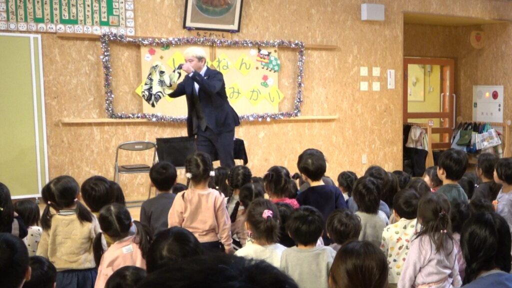 ステージ上でマジシャン・コンプレッサーがゾンビボール マジックを演じている瞬間。園児たちが真剣な表情で見つめている。