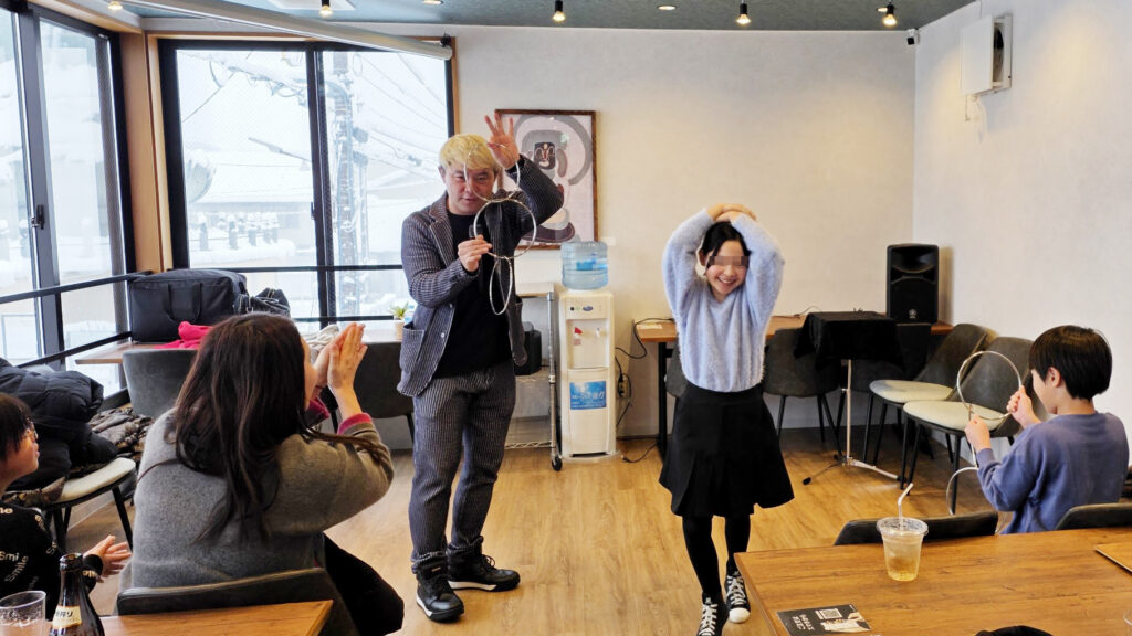 新年会のマジックショーで、お子さんと一緒にチャイニーズステッキやリングのマジックで盛り上がる会場の様子