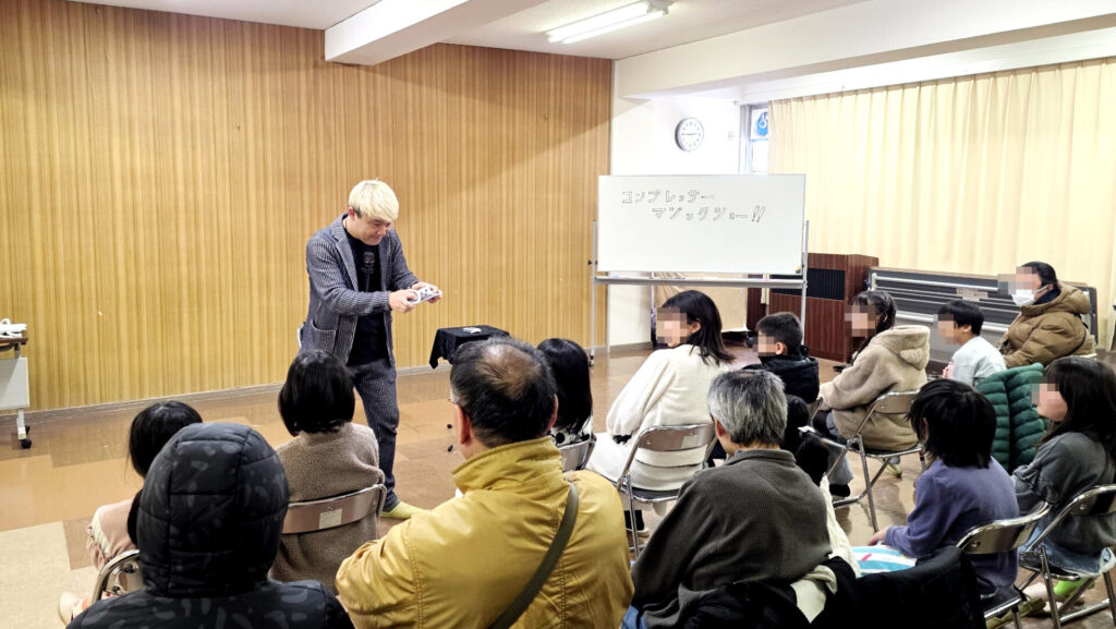 マジシャン・コンプレッサーのマジックショーに見入る児童クラブの親子