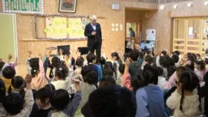 保育園の新年お楽しみ会でマジシャン・コンプレッサーのショーに園児が一斉に手を挙げる様子