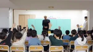 学童保育のマジックショーで子どもたちが一斉に手を挙げて盛り上がる様子