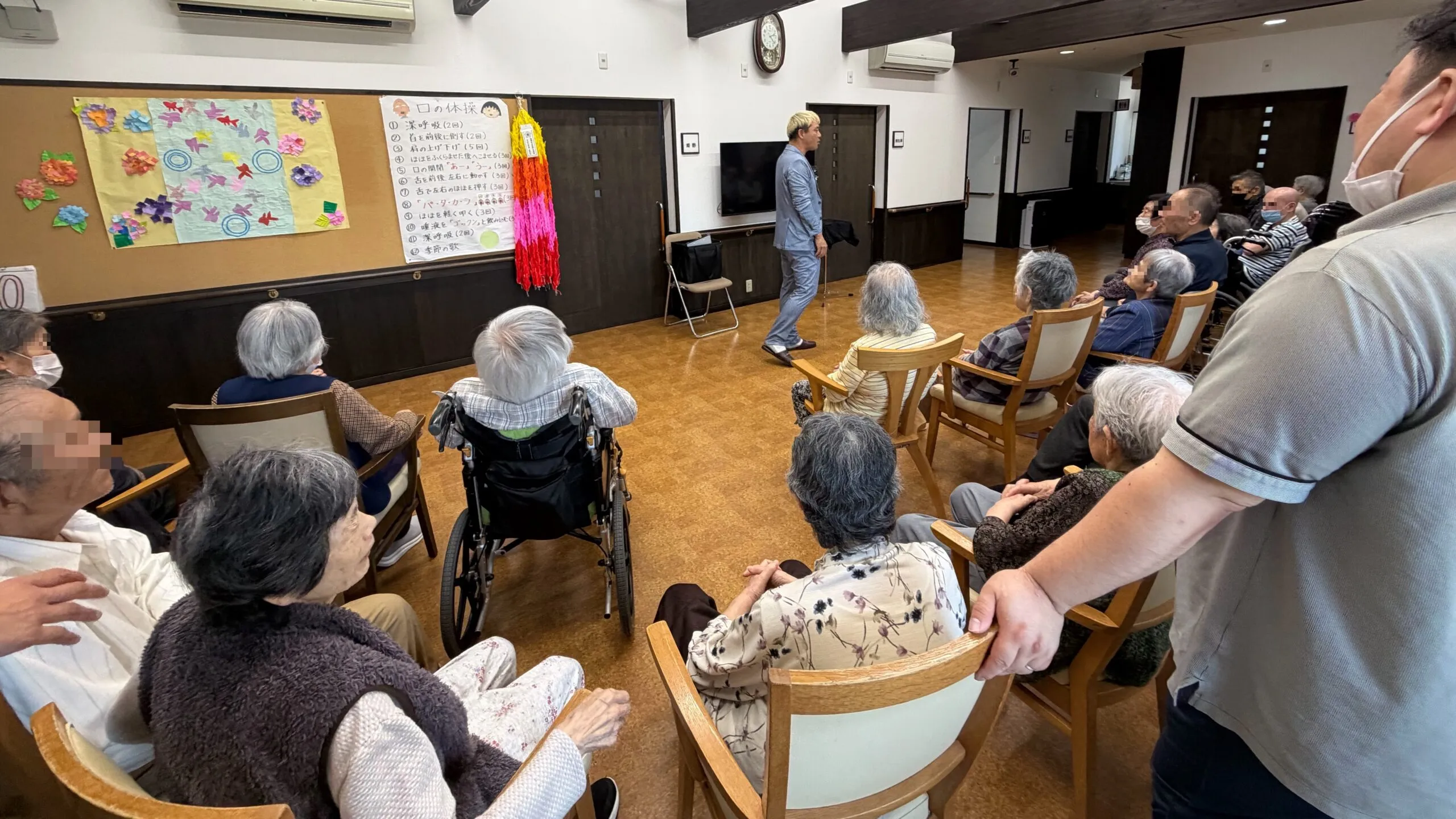 ケアホームなかそねのフロア。テレビや手作りの折り紙飾りに囲まれた団らんの場所でマジックショーの準備をする様子