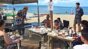 富山県氷見市の海の家で開かれたバーベキューの余興として、砂浜のテント下でテーブルマジックを披露するマジシャン・コンプレッサー