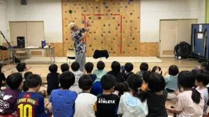 富山県氷見市の学童保育のホールで、床に座った子どもたちの前でマジックを演じるマジシャン・コンプレッサー