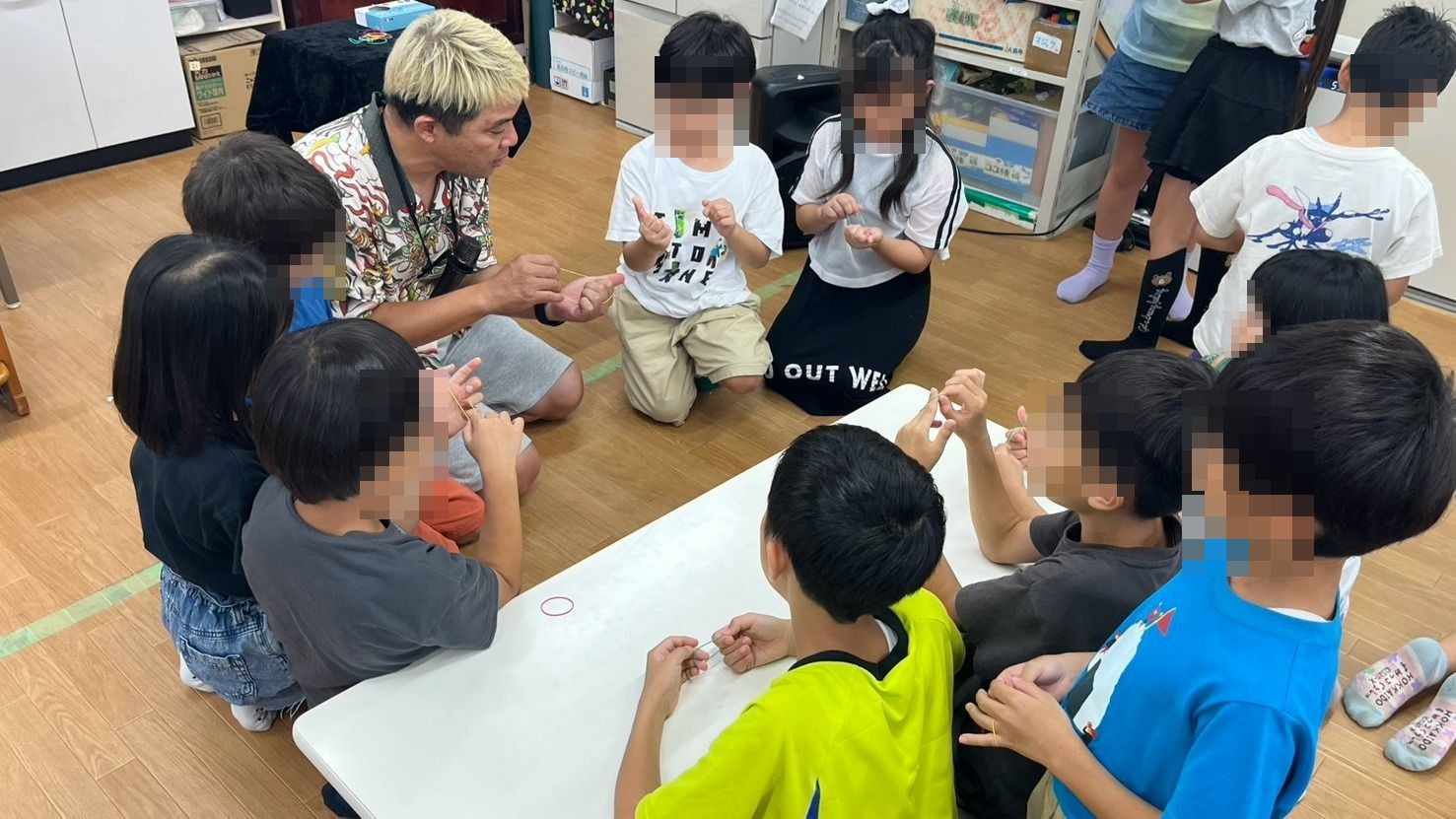 石川県白山市の学童保育でテーブルを囲み輪ゴムのマジックを教わる子どもたち