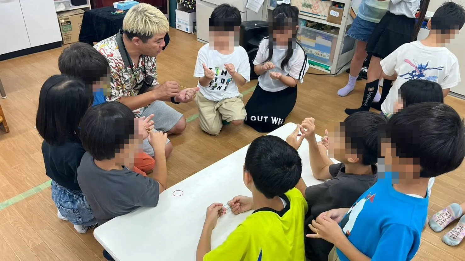 石川県白山市の学童保育でテーブルを囲み輪ゴムのマジックを教わる子どもたち