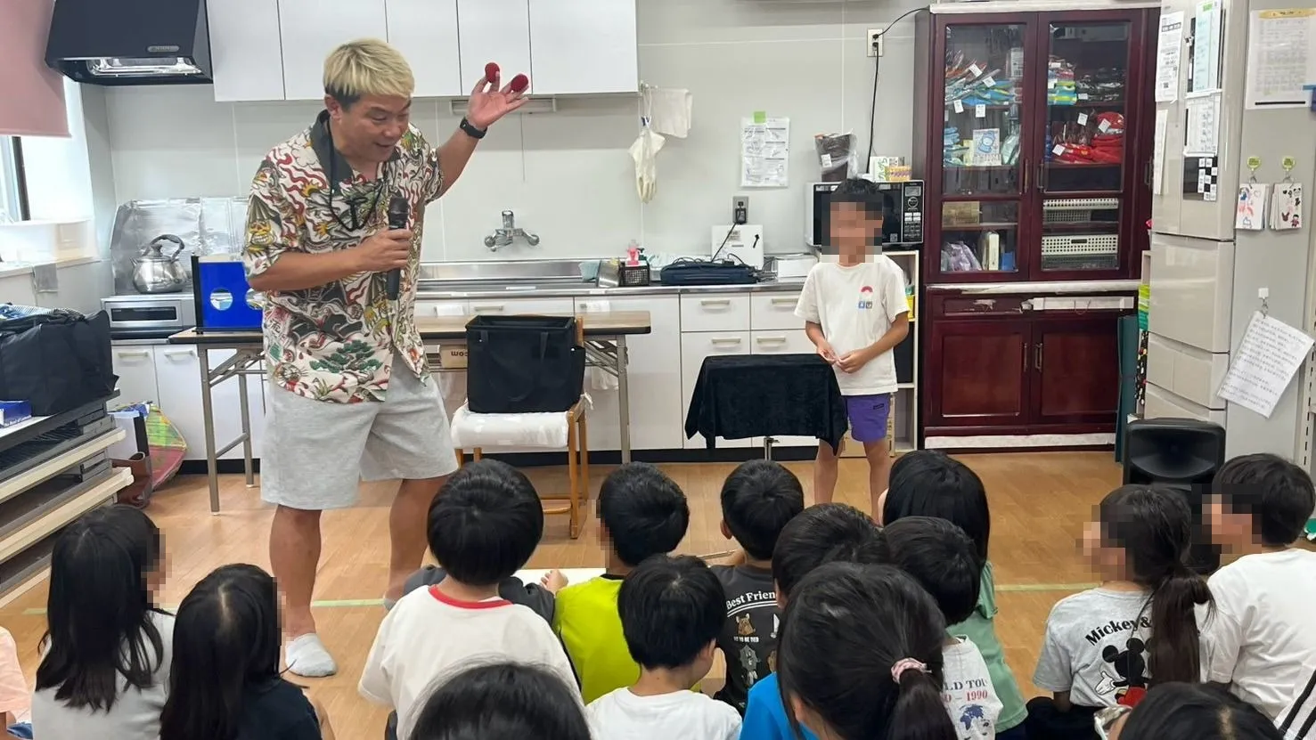 石川県白山市の学童保育のマジックショーで赤いスポンジボールを掲げ、舞台に上がった子どもとやりとりするマジシャン・コンプレッサー