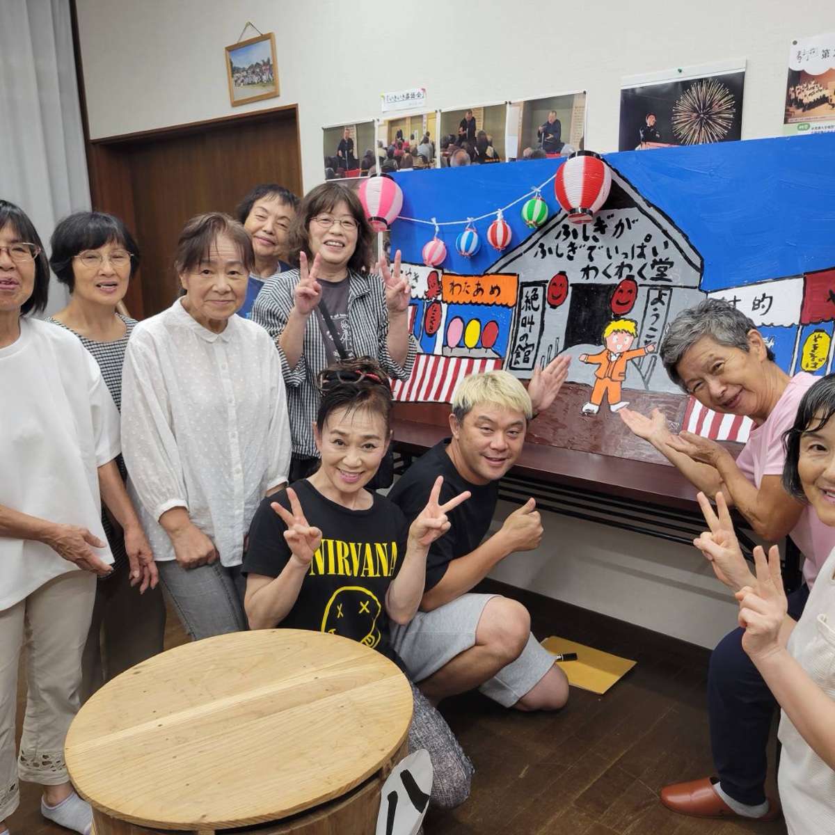 氷見「愛の劇団」の稽古場で新作『氷見のお祭り』の縁日背景幕を囲む団員の皆さん