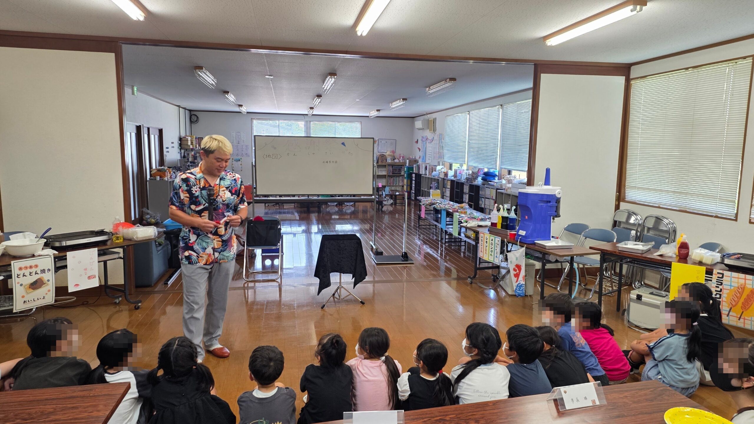 氷見市のビバふじみだい児童育成クラブ10周年記念行事で手作りのお店が並ぶ会場とマジックショーを見る子どもたち