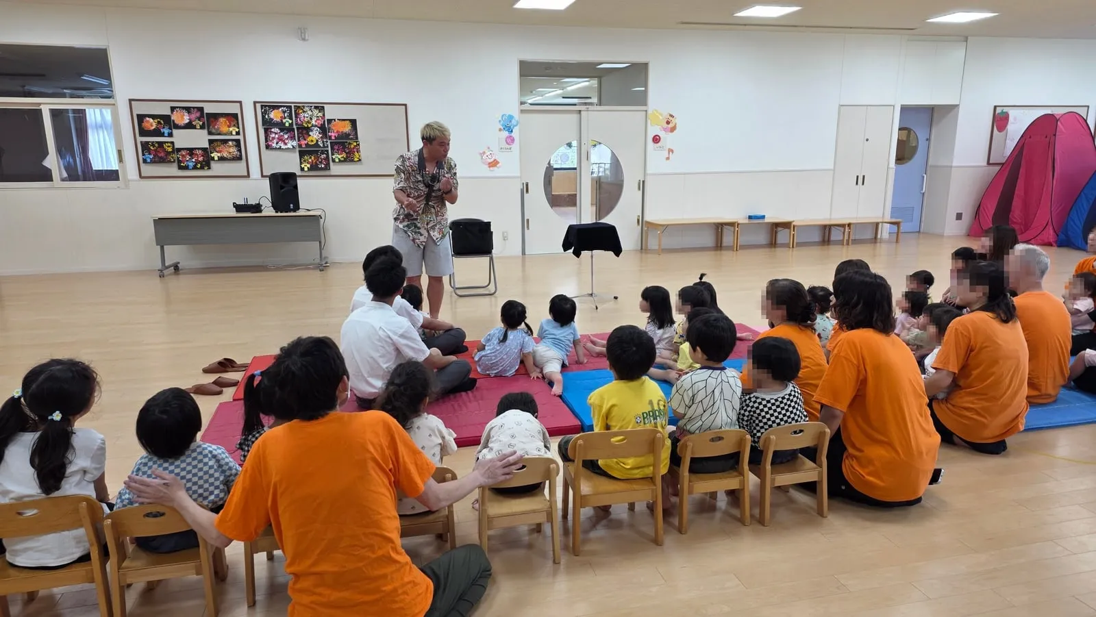 富山市の保育園のプレイルームでマットに座った0歳から5歳の園児さんがマジックショーを見ている様子