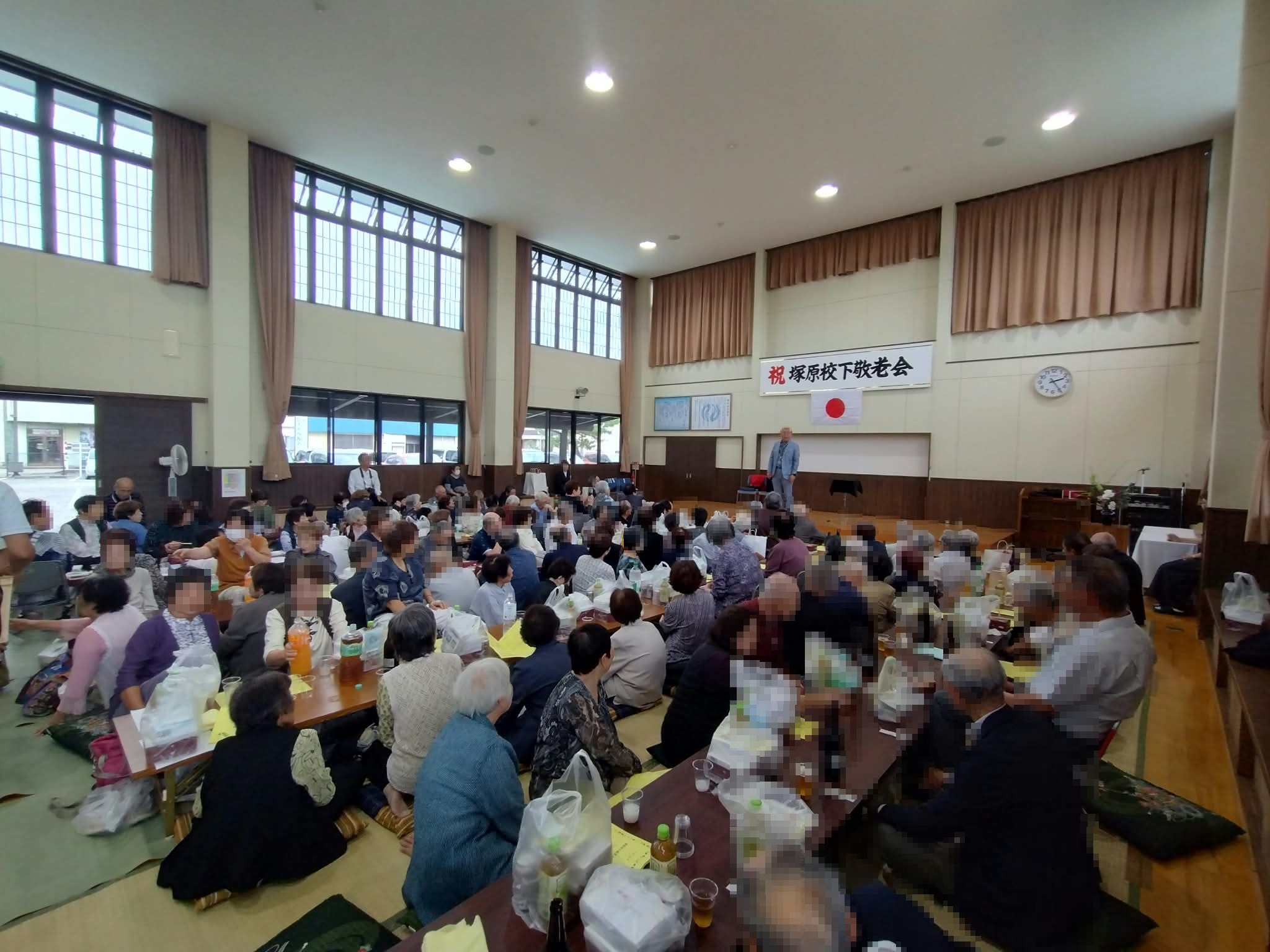 射水市の敬老会の会場後方から見た、テーブルを囲んで座る客席とステージのマジックショー