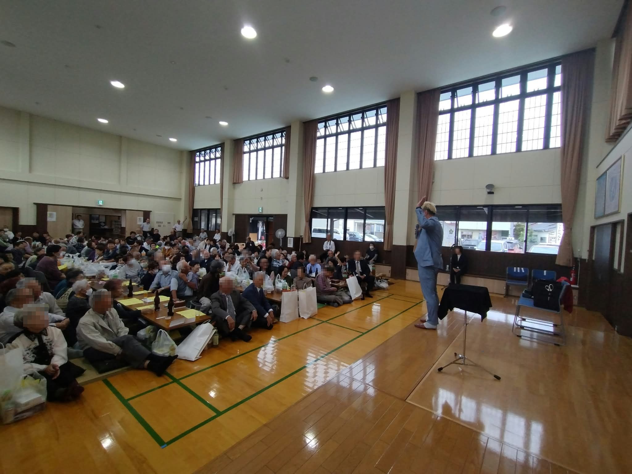 射水市の敬老会で片手を高く挙げてマジックショーを盛り上げるコンプレッサーと客席