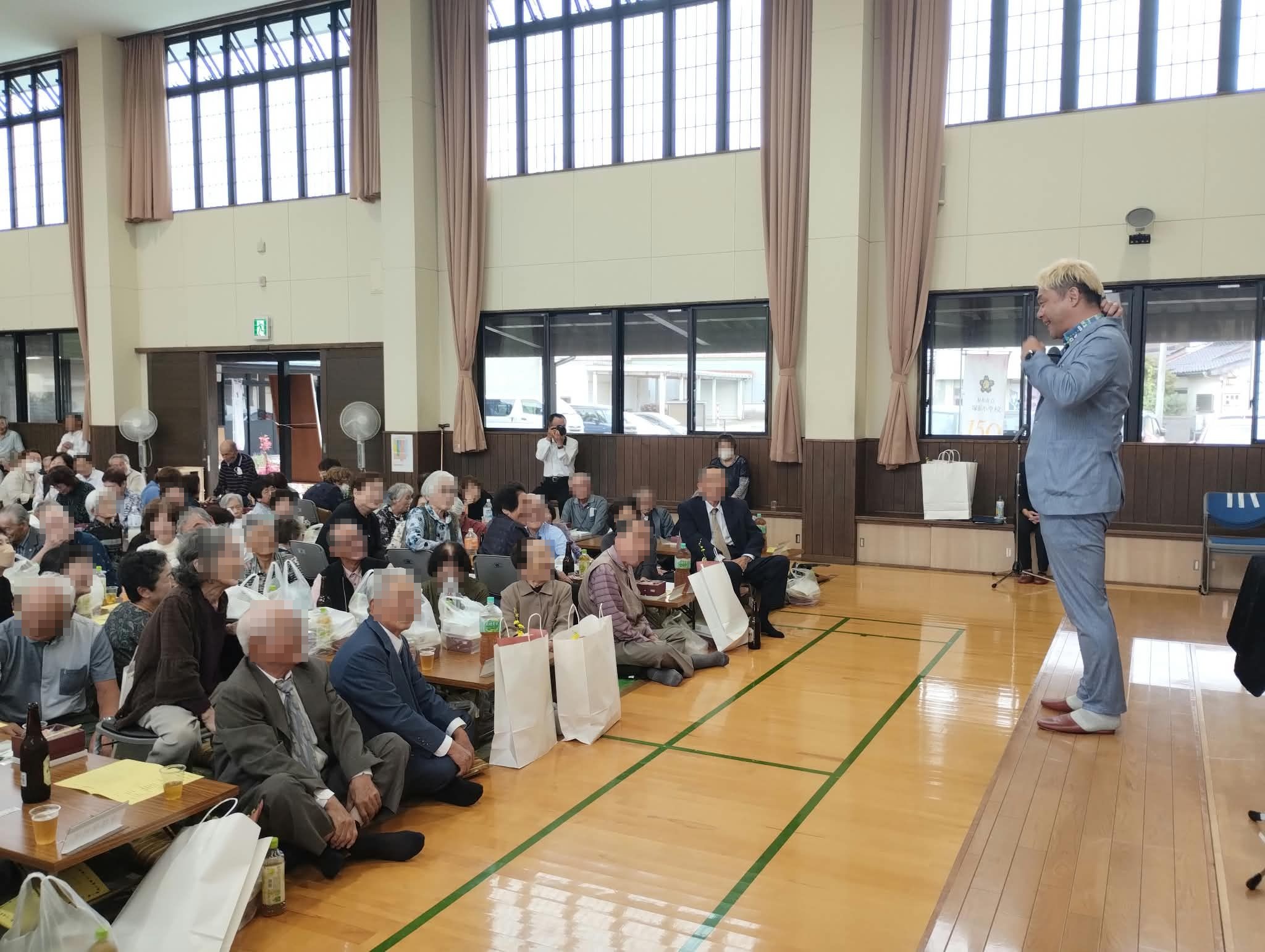 射水市の敬老会でステージの端に立ち、最前列のお客さんに語りかけるコンプレッサー