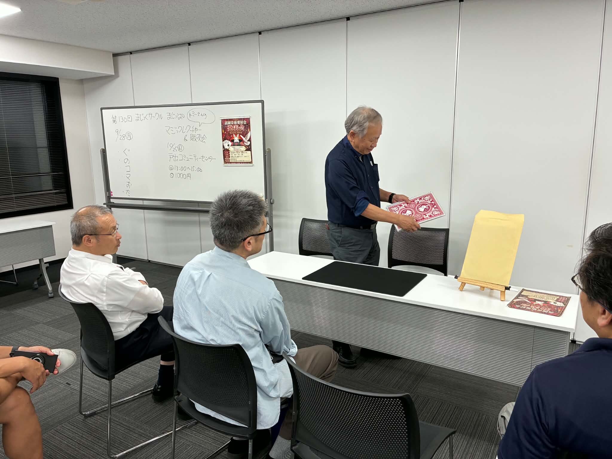 射水市のQQプラザの会議室で、大きなカードを見せながらマジックを演じるまじっぱのメンバー｜富山のマジックサークル
