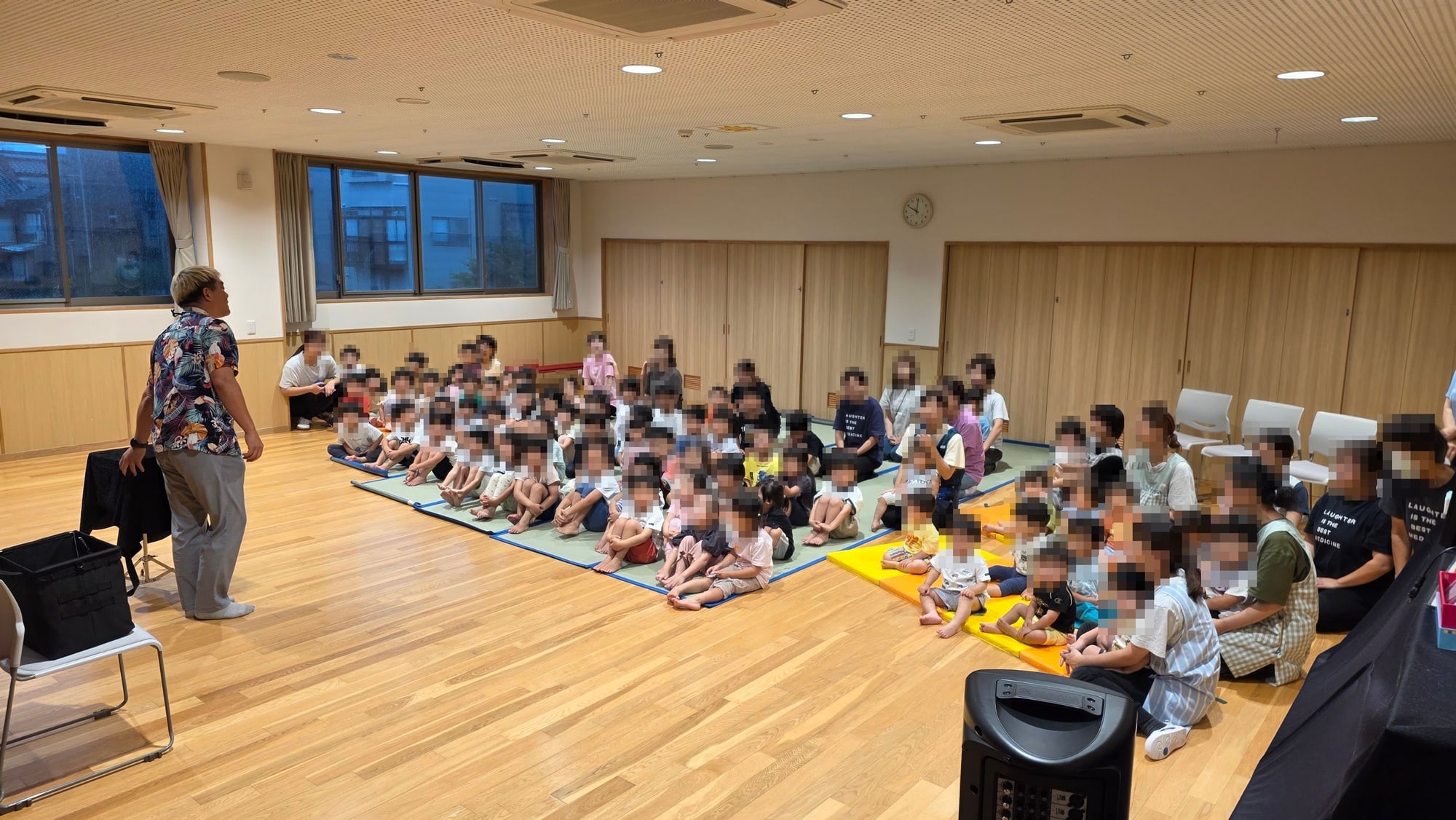 保育園のホールでマジックショーがはじまり、床に座った子どもたちが見つめている