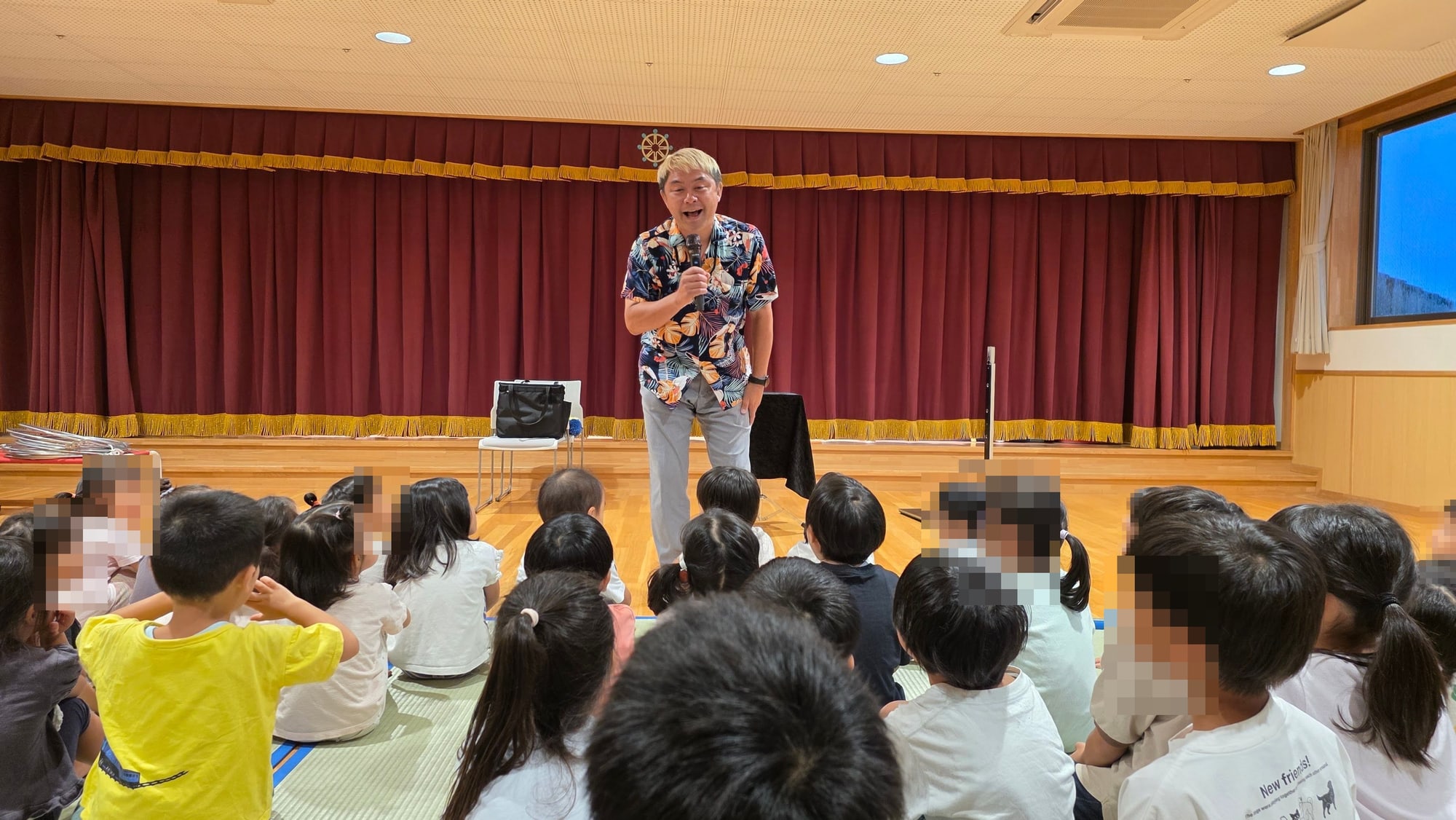 保育園のホールでマイクを持って笑うマジシャン コンプレッサー