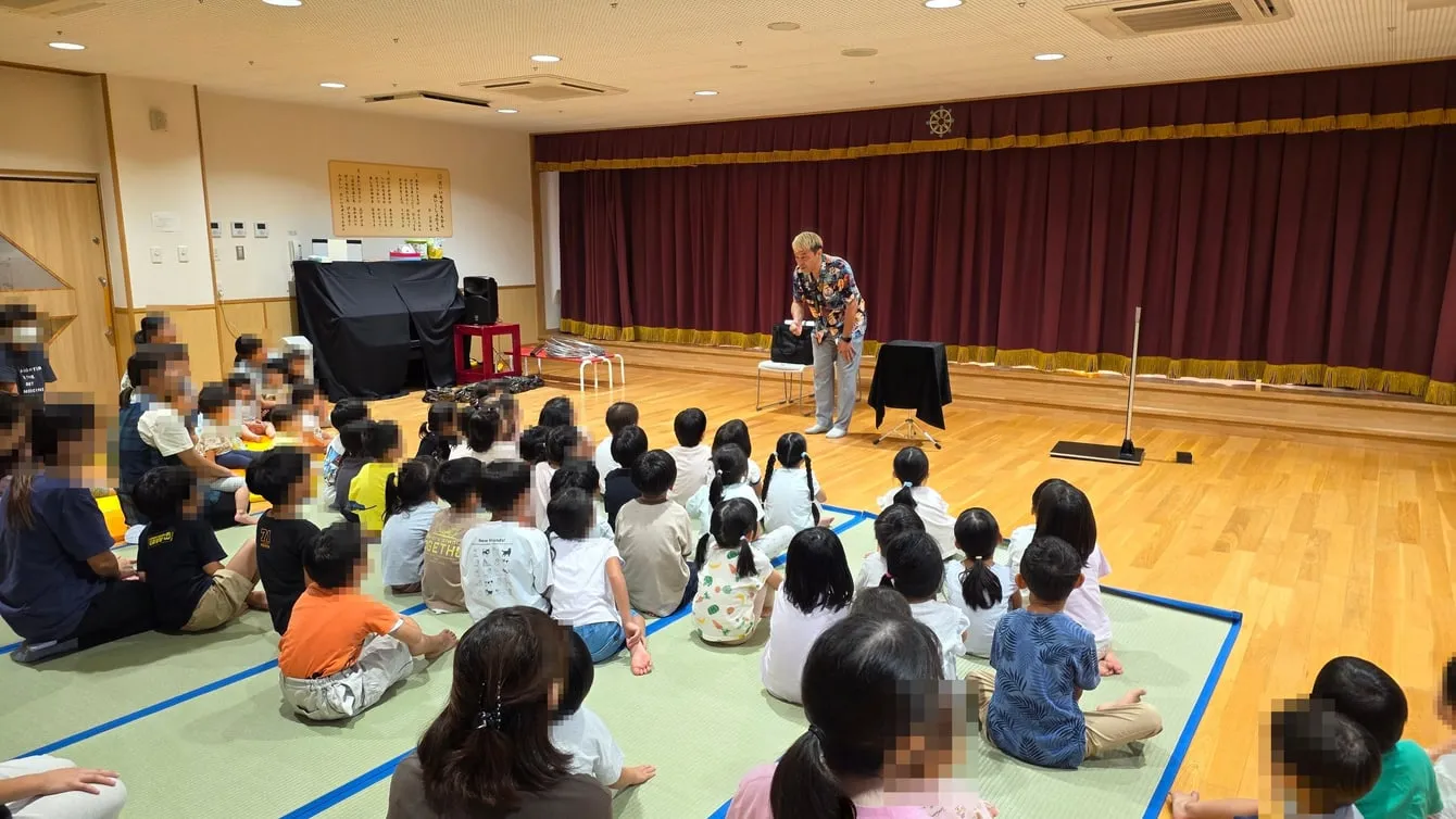 保育園のホールの床で、子どもたちの前でマジックショーを進めるコンプレッサー