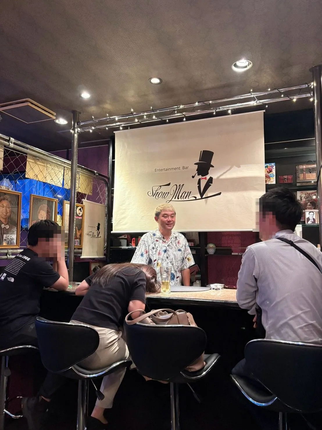 富山市桜木町のマジックバー ショーマンのカウンターで、アロハシャツのマジシャン・コンプレッサーがお客さまにマジックを披露する様子
