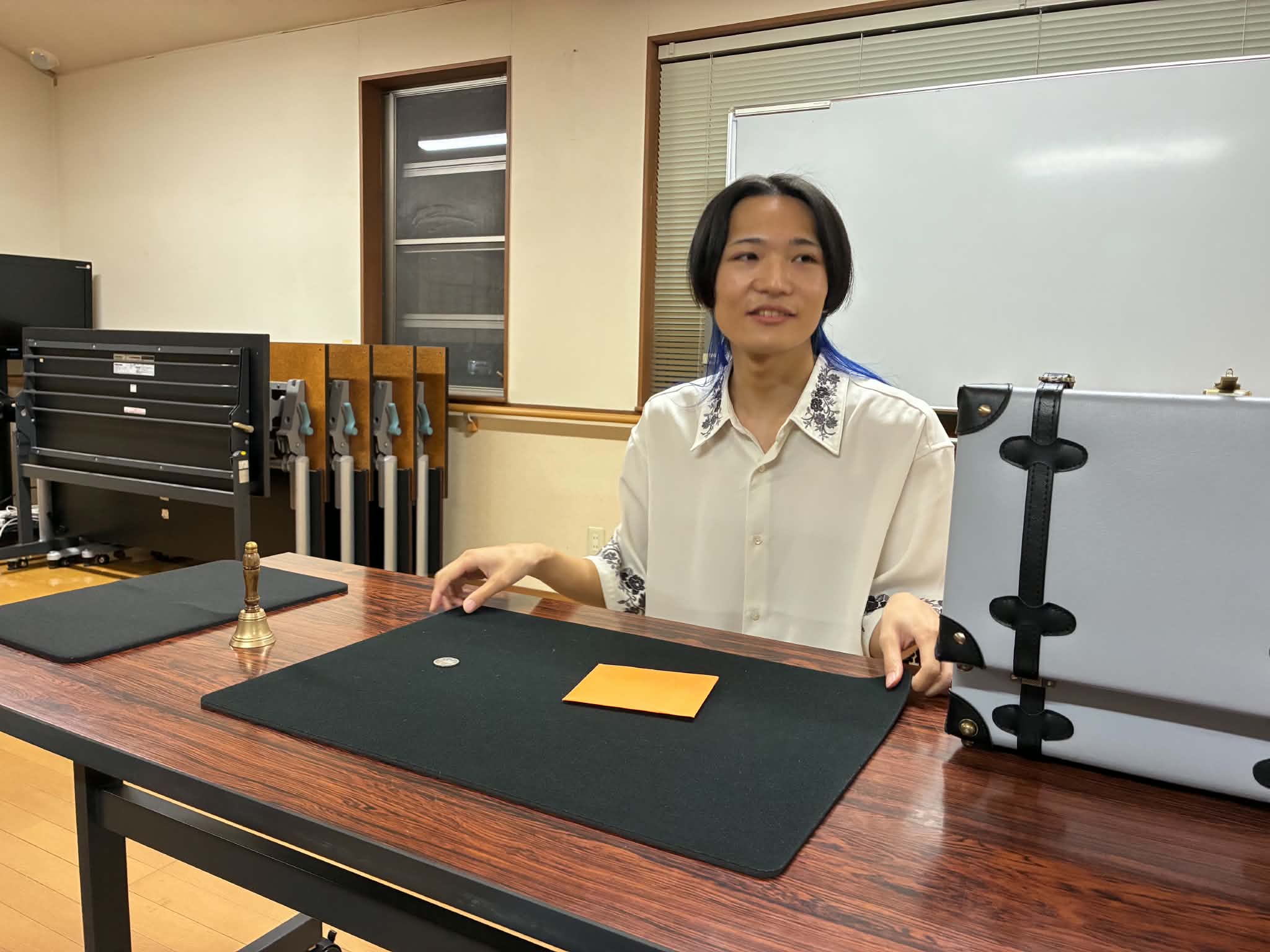 マジック研究会のネタ見せでテーブル上のコインと封筒を使って演じる所属マジシャン