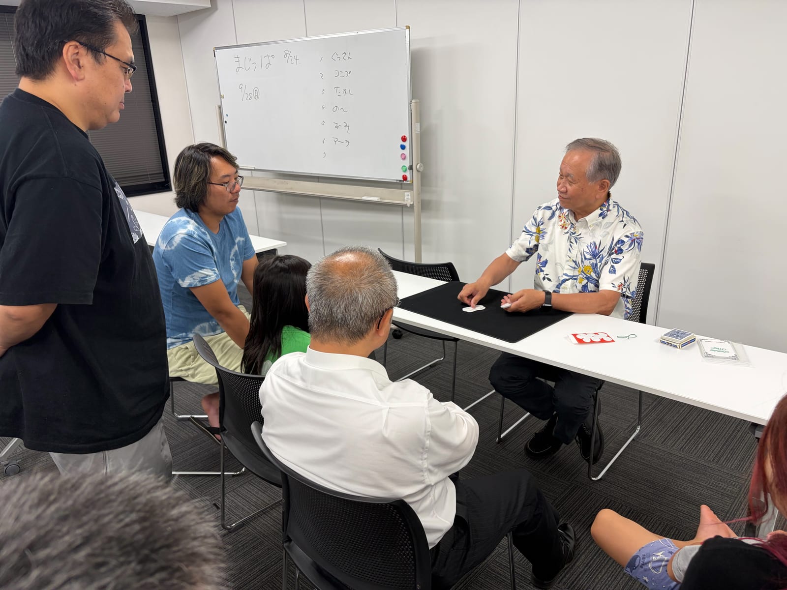 富山のマジックサークルを見学したご家族の夜|まじっぱ8月24日レポート 5 花柄のアロハシャツのベテランメンバーがカードで場を沸かせ、大きな口を開けて笑う男の子と輪になる家族連れの見学者|富山マジックサークルまじっぱ
