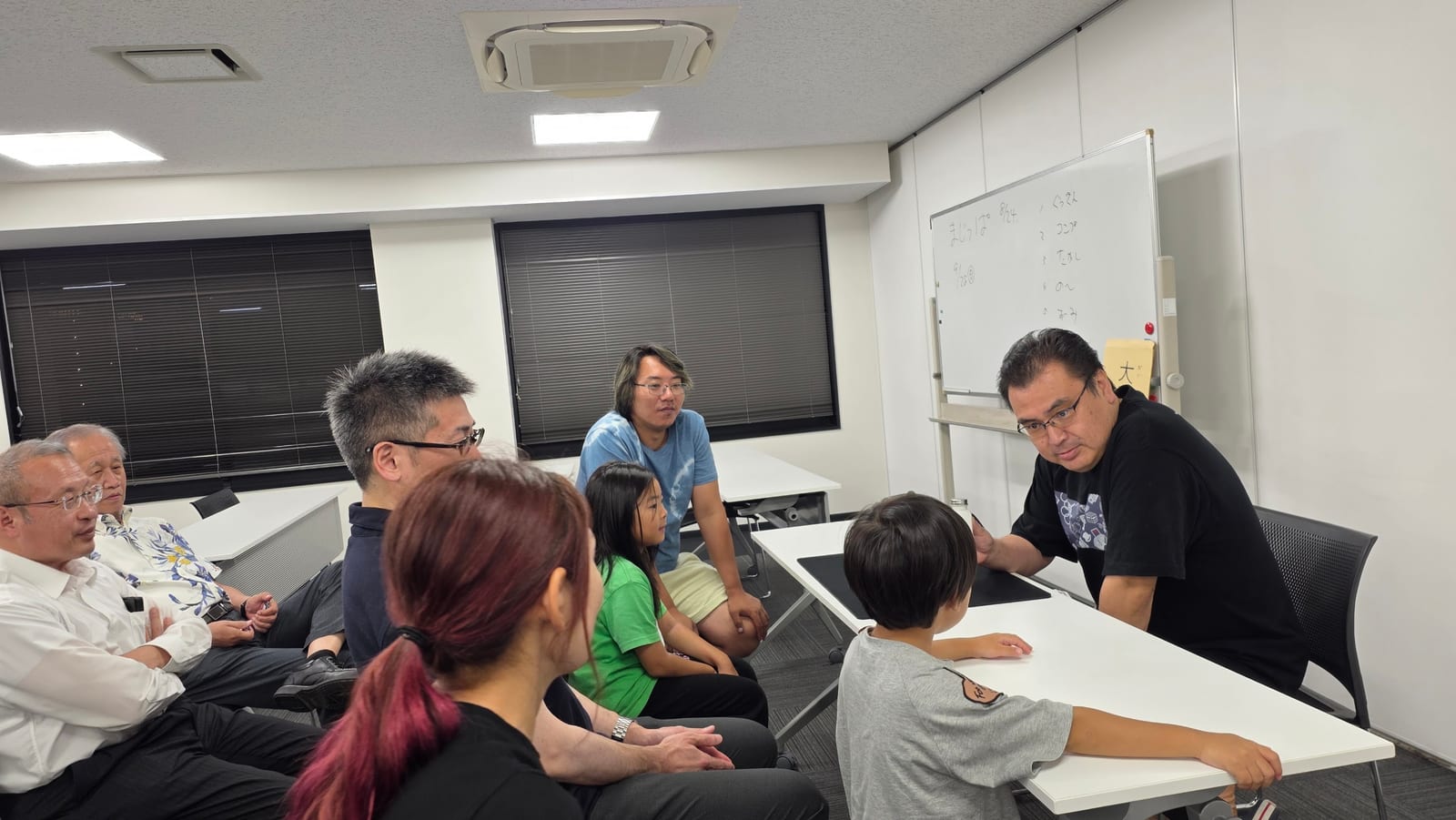 富山のマジックサークルを見学したご家族の夜|まじっぱ8月24日レポート 4 黒いTシャツのメンバーが息子さんとテーブル越しにマジックを演じ、見学のご家族が輪になって見守る様子|富山マジックサークルまじっぱ