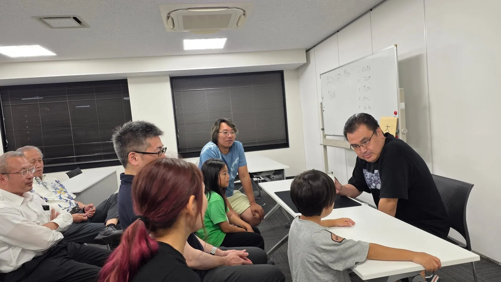 富山のマジックサークルを見学したご家族の夜|まじっぱ8月24日レポート 4 黒いTシャツのメンバーが息子さんとテーブル越しにマジックを演じ、見学のご家族が輪になって見守る様子|富山マジックサークルまじっぱ
