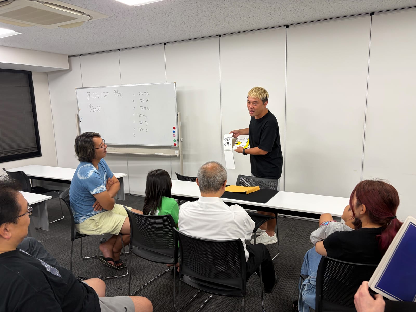 富山のマジックサークルを見学したご家族の夜|まじっぱ8月24日レポート 6 金髪の若手メンバーが手描きのイラストマジックを見せ、見学の娘さんと会場全員が視線を集中させる様子|富山マジックサークルまじっぱ
