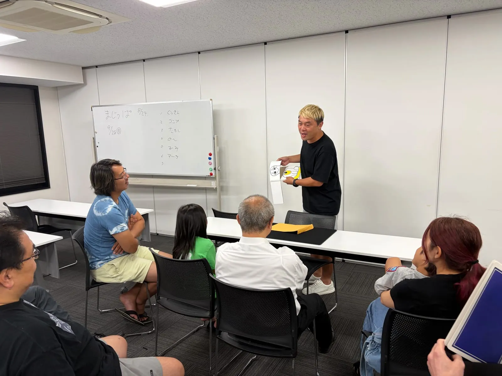 富山のマジックサークルを見学したご家族の夜|まじっぱ8月24日レポート 6 金髪の若手メンバーが手描きのイラストマジックを見せ、見学の娘さんと会場全員が視線を集中させる様子|富山マジックサークルまじっぱ
