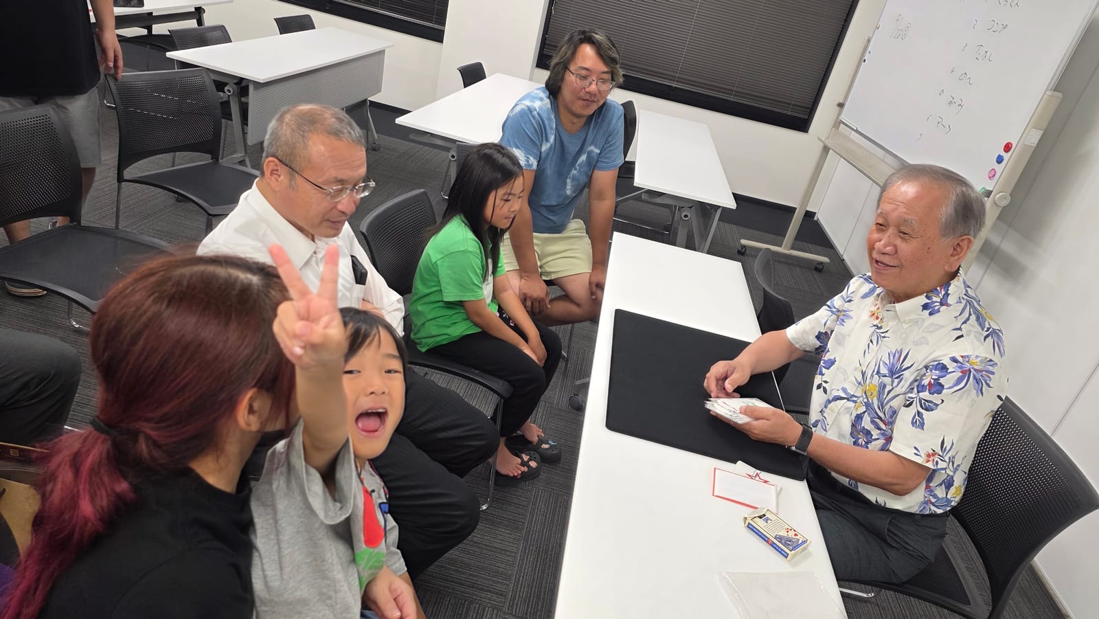 富山のマジックサークルを見学したご家族の夜|まじっぱ8月24日レポート 3 花柄のアロハシャツで座ってカードマジックを演じるベテランメンバーと囲むまじっぱの仲間たち|富山マジックサークル